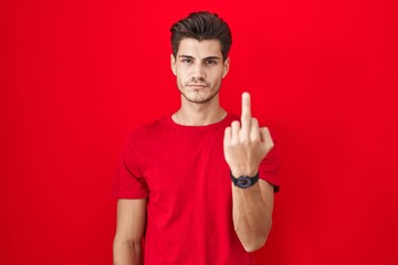 Sticker - Young hispanic man standing over red background showing middle finger, impolite and rude fuck off expression