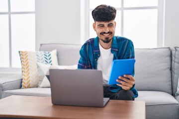 Sticker - Young hispanic man using laptop and touchpad sitting on sofa at home