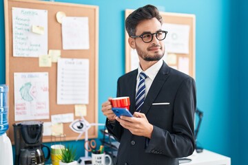 Poster - Young hispanic man business worker using smartphone drinking coffee at office