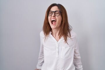 Poster - Brunette woman standing over white isolated background angry and mad screaming frustrated and furious, shouting with anger. rage and aggressive concept.