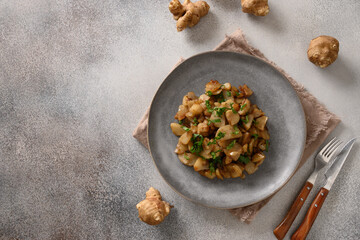 Roasted topinambur, sunchokes with garlic and parsley on gray background. View from above. Copy space.