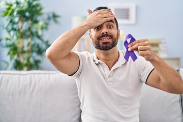 Sticker - Young hispanic man with beard holding purple ribbon awareness stressed and frustrated with hand on head, surprised and angry face