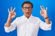 © Krakenimages.com - Middle age hispanic man standing over blue background looking surprised and shocked doing ok approval symbol with fingers. crazy expression