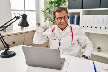 Poster - Senior doctor man working on online appointment smiling doing phone gesture with hand and fingers like talking on the telephone. communicating concepts.