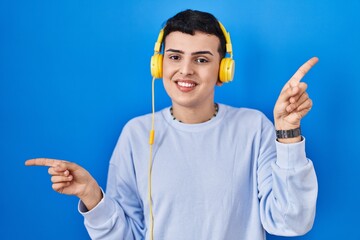 Poster - Non binary person listening to music using headphones smiling confident pointing with fingers to different directions. copy space for advertisement