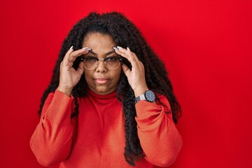 Poster - Plus size hispanic woman standing over red background trying to open eyes with fingers, sleepy and tired for morning fatigue