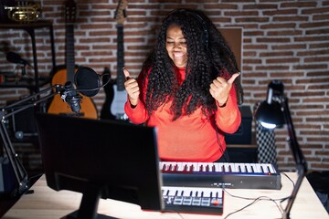 Poster - Plus size hispanic woman playing piano at music studio success sign doing positive gesture with hand, thumbs up smiling and happy. cheerful expression and winner gesture.