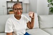 © Krakenimages.com - Senior african american woman holding denture sitting on sofa at home