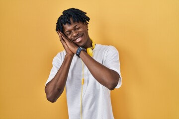 Sticker - Young african man with dreadlocks standing over yellow background sleeping tired dreaming and posing with hands together while smiling with closed eyes.