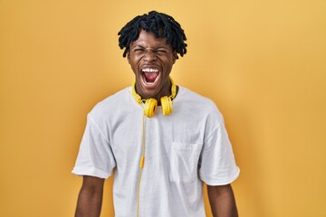 Sticker - Young african man with dreadlocks standing over yellow background angry and mad screaming frustrated and furious, shouting with anger. rage and aggressive concept.