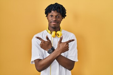 Young african man with dreadlocks standing over yellow background pointing to both sides with fingers, different direction disagree