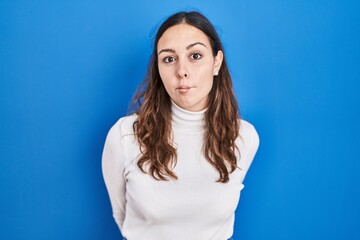 Sticker - Young hispanic woman standing over blue background making fish face with lips, crazy and comical gesture. funny expression.