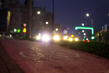 Bike Sign On The Sidewalk With Red Background And Car Lights