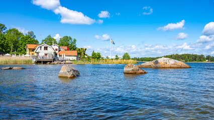 Sunny day in a small village bay on Vaxholm Island. On the coast is the Hembygdsgard Museum and a tranquil terrace with seating areas for guests. Stockholm Archipelago, Sweden