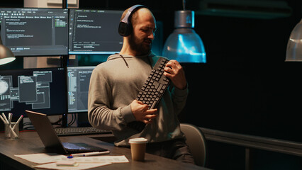 Programmer being happy and playing air guitar with keyboard instrument, enjoying music or song and having fun. Young cheerful adult acting silly fooling around late at night in office.