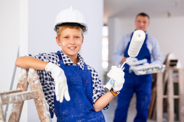 Wall Mural - Smiling boy in coverall holding paint roller. Youngster assisting with home improvement works.