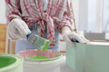 Canvas Print - Woman dipping brush into bucket of green paint at table indoors, closeup