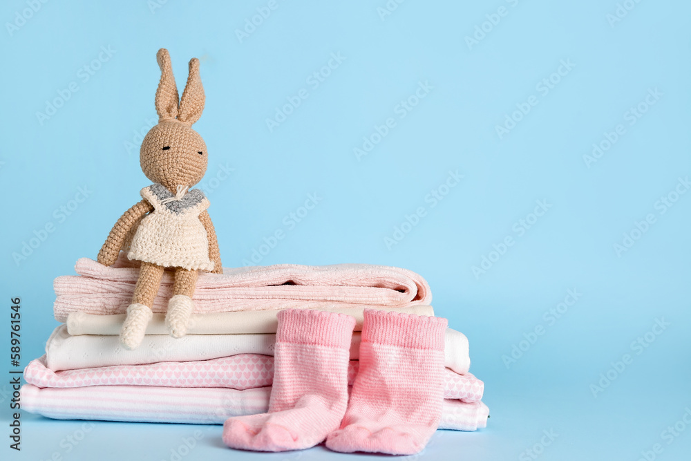 Stack of baby clothes, socks and toy on color background