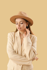 Poster - Fashionable young woman in stylish jacket and hat on beige background