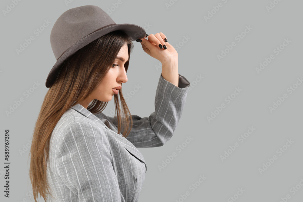 Stylish young woman in jacket and hat on grey background