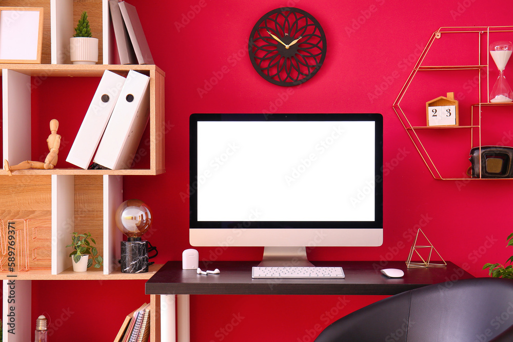 Workplace with computer and earphones near red wall in office