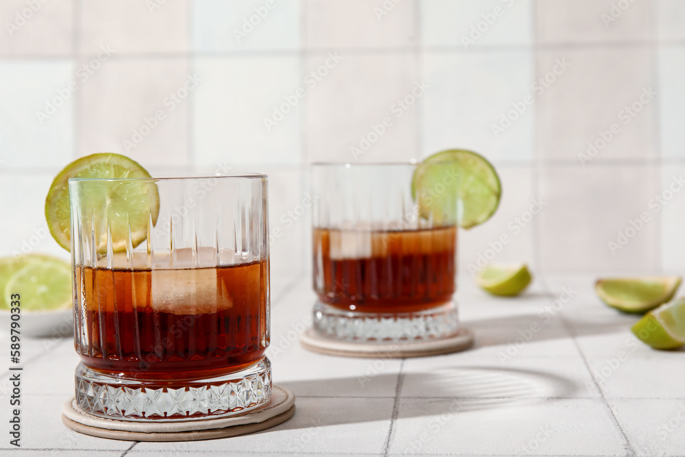 Glasses of cold rum with lime on white tile background