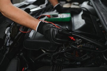 Car mechanic is using a multimeter with voltage range measurement to check the voltage level of the car battery.