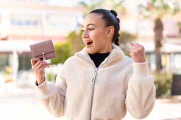 Wall Mural - Young moroccan girl holding a wallet at outdoors celebrating a victory