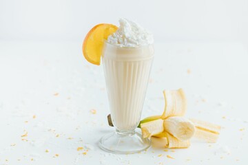 Wall Mural - Closeup shot of a tall glass cup of banana milkshake topped with whipped next to banana