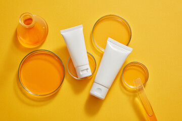 Top view of two white tube arranged with petri dishes, a test tube and an erlenmeyer flask containing orange liquid. Natural skin care beauty product advertising