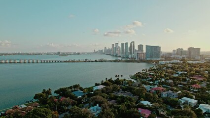 Canvas Print - Aerial view of a city with green vegetation at the shore at calm sunset