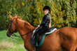 Little girl in jockey outfit rides bay horse. School of riding and equestrian sports.
