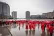 Crowd of all kind of people walking on a plaza fast moving in red rain coats from the back with blurry buildings, red movement