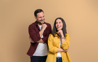 Wall Mural - Romantic young man looking at beautiful girlfriend smiling with hand on chin. Happy attractive couple dressed in casuals posing cheerfully while standing against beige background