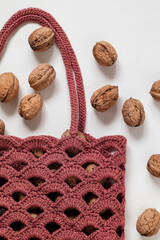 Wall Mural - Burgundy crochet mesh bag with whole walnuts on a white background.