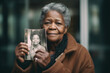 © Trinette Reed - Senior black woman holding up a vintage photo of herself when she was younger. Generative AI.