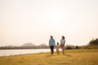 © Kiattisak - Happy Family enjoying a peaceful walk and running in a scenic field with a serene lake in the background.