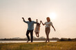 © Kiattisak - Happy Family enjoying a peaceful walk and running in a scenic field with a serene lake in the background.
