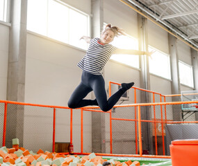 Wall Mural - Pretty girl in trampoline park jumping with split and smiling. Happy teenager enjoying amusement activities