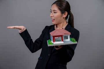 young asian woman wearing formal suit, holding and showcasing house model on isolated background. id