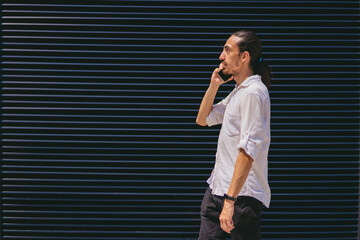 young latin long haired man in shirt talking on cell phone while walking down the street. copy space