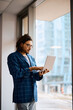 © Drazen - Latin American businesswoman using laptop by window in office.