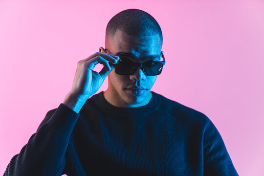 confident young man wearing sunglasses and a black sweater on pink background, studio shot. high qua