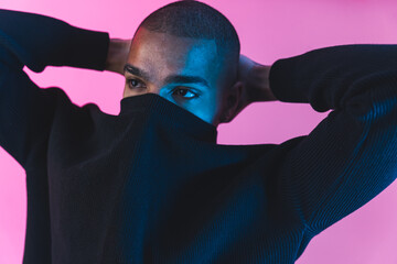 unrecognisable incognito male model with face covered by his black hoodie over pink background. face