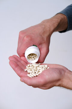 male hand spilling, stretches on palm white pills or vitamins, capsule on blurred light background, 