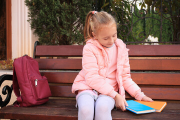 cute little girl with backpack and books on bench outdoors