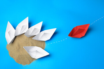 Wall Mural - Red paper boat floating away from others on light blue background, flat lay. Uniqueness concept