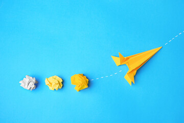 Poster - Handmade orange rocket and crumpled pieces of paper on light blue background, flat lay with space for text