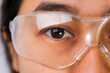 © Pornpimon - Close-up of woman's eye wearing transparent safety glasses. Asian woman wearing protective goggles.