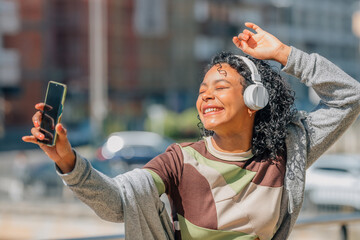 Wall Mural - latin girl with afro hair with headphones and mobile phone in the street